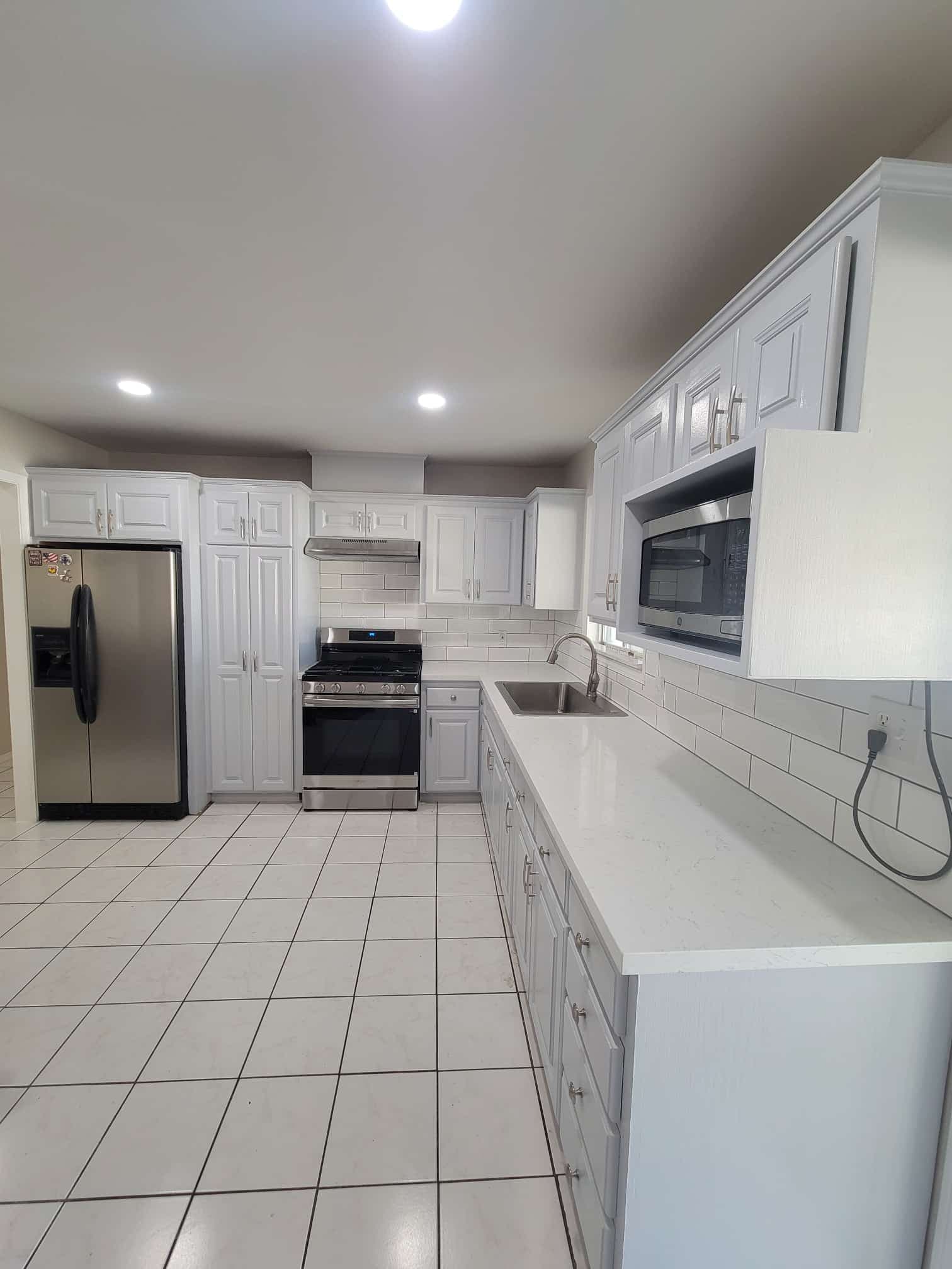 Modern kitchen with white cabinets, stainless steel appliances, and tile flooring.