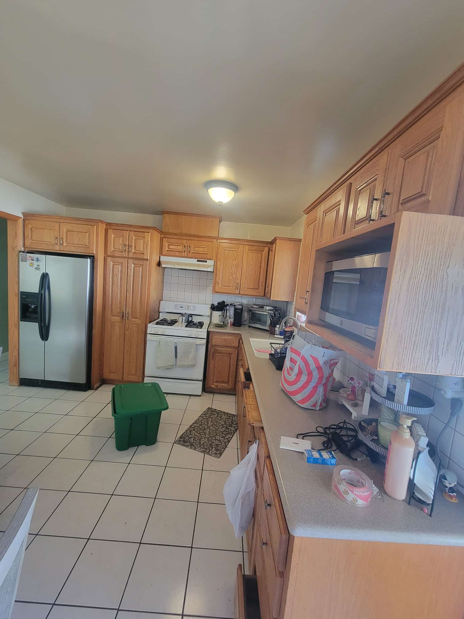 Spacious kitchen with oak cabinetry, tile flooring, appliances, and a green storage box.