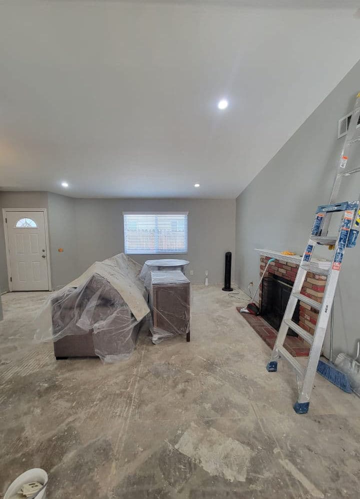 Living room under renovation with furniture covered, ladder, and gray walls.