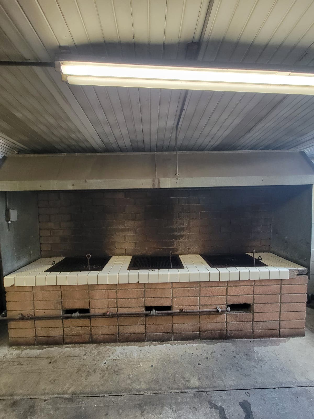Outdoor grill station with brick structure and tiled countertop, featuring three grilling areas.