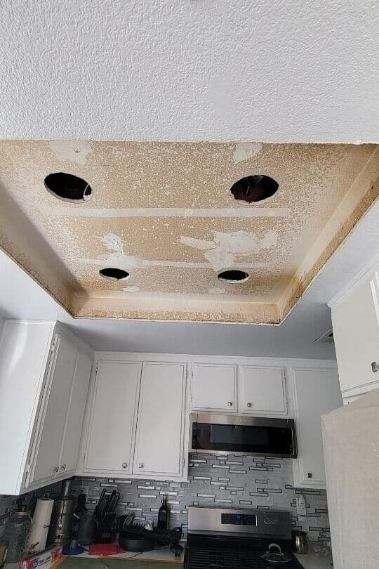 Damaged kitchen ceiling with exposed holes and peeling paint, showing unfinished renovation.