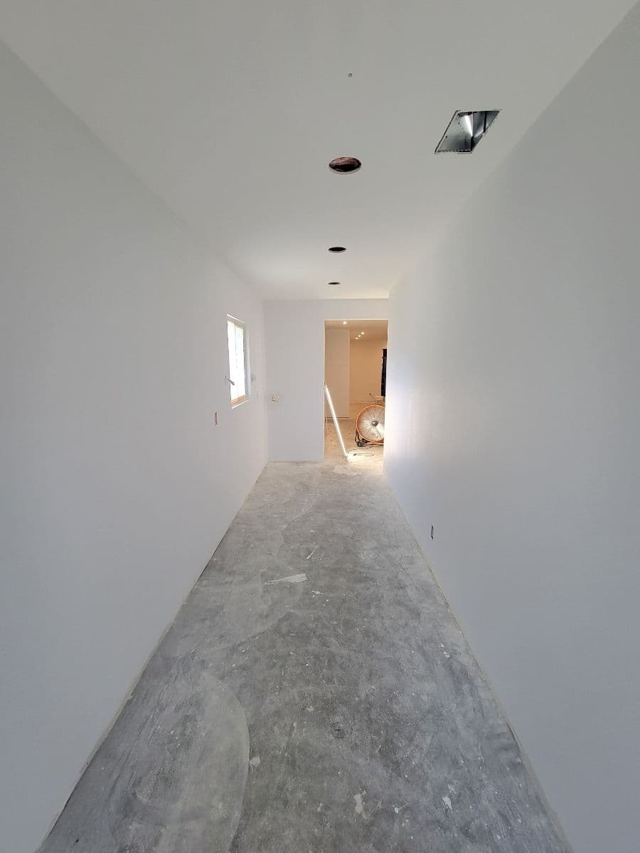 Empty interior hallway with white walls and unfinished floor, showing construction progress.