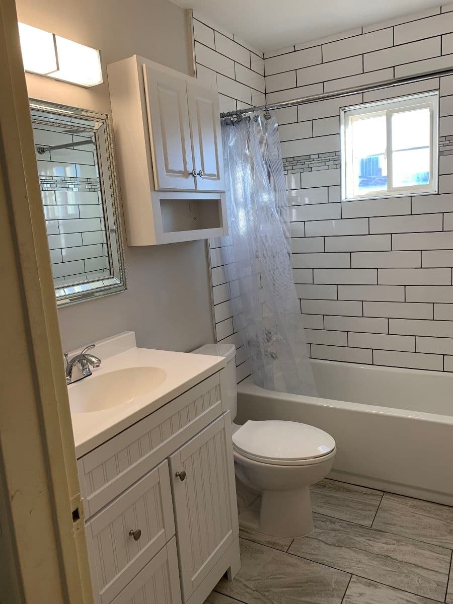 Modern bathroom with white tile, shower curtain, and stylish vanity with storage.