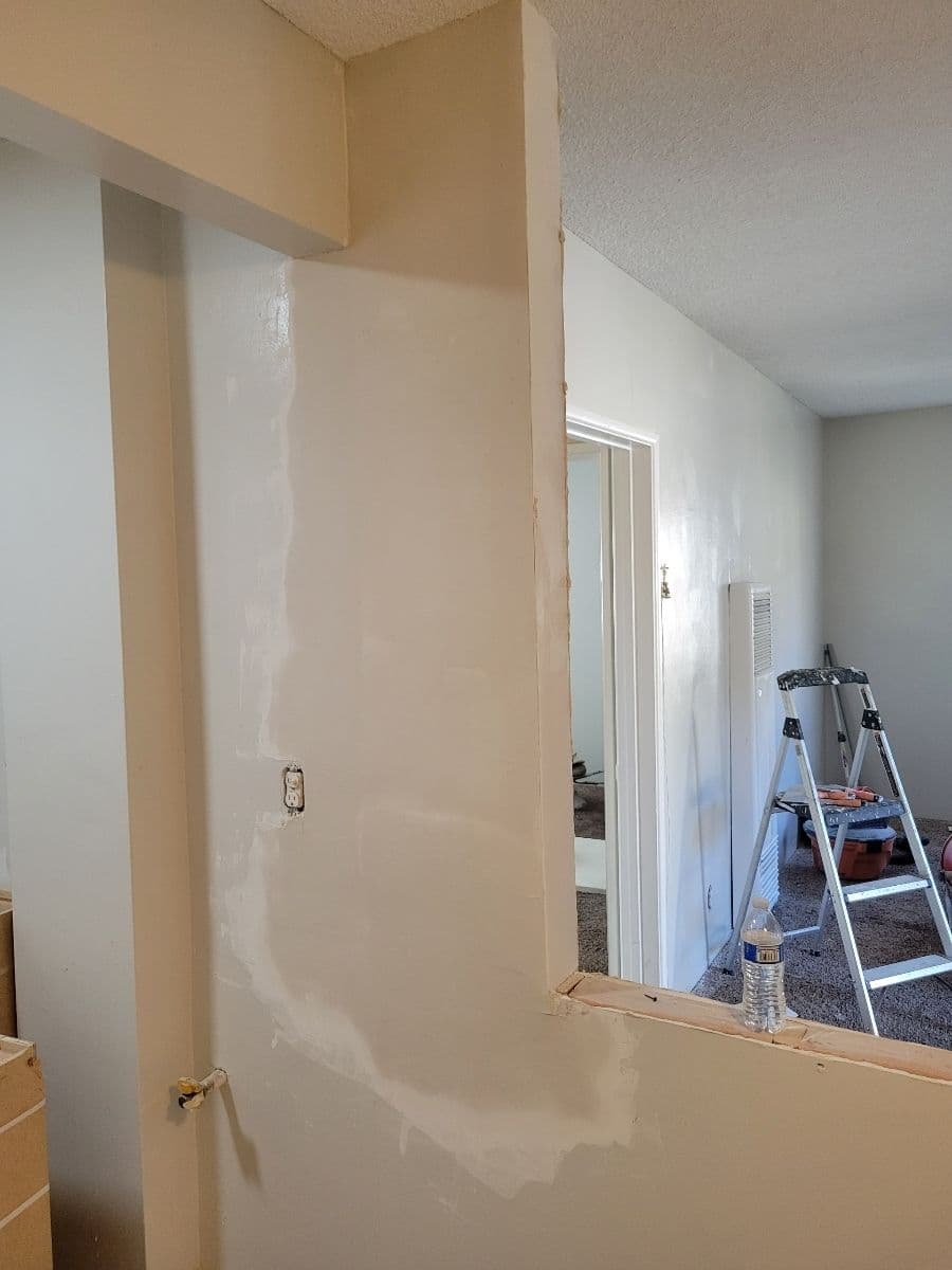 Interior wall undergoing renovation with fresh plaster, ladder, and construction tools visible.