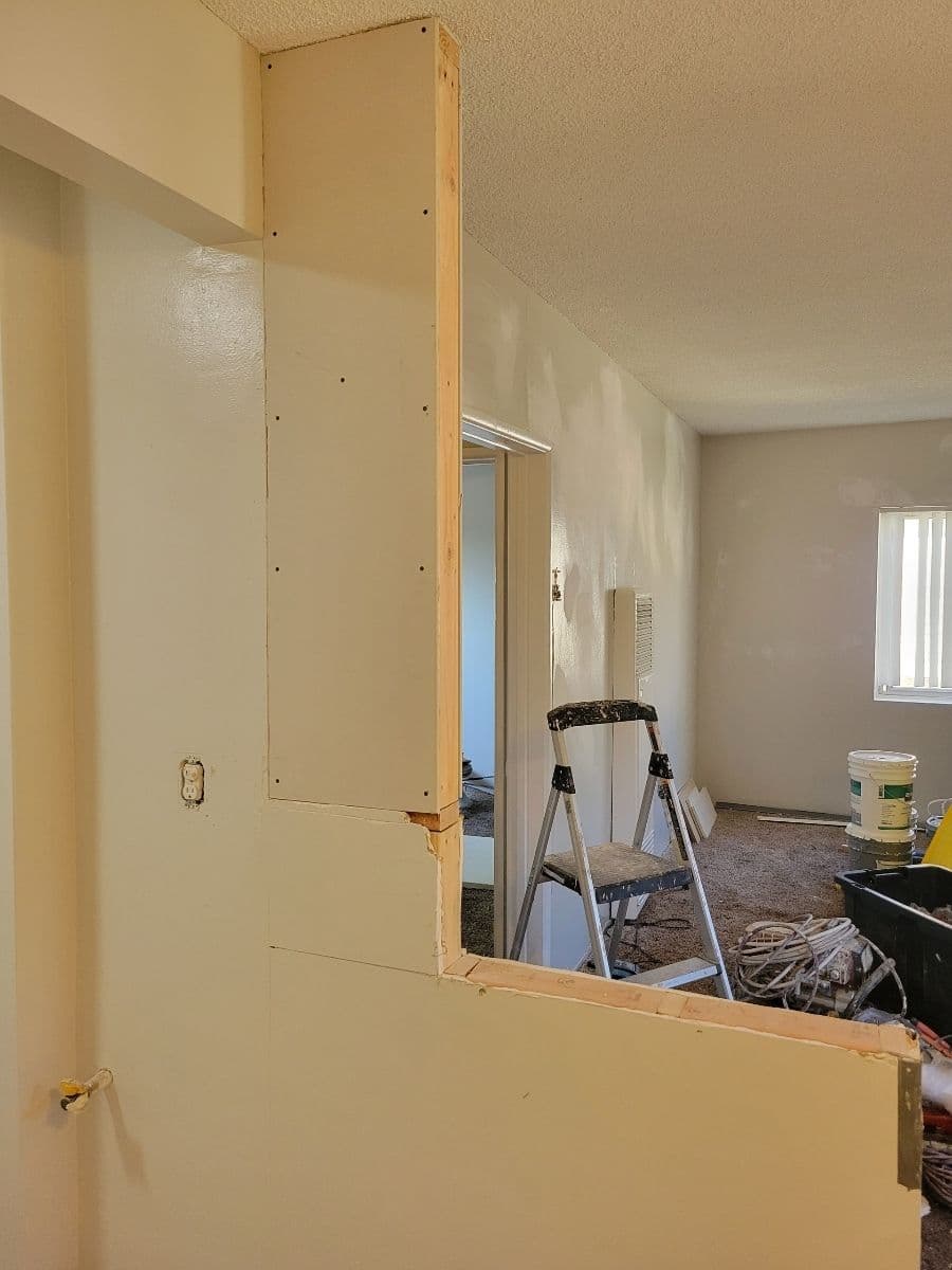 Drywall installation in a renovated room with construction tools and ladder in view.