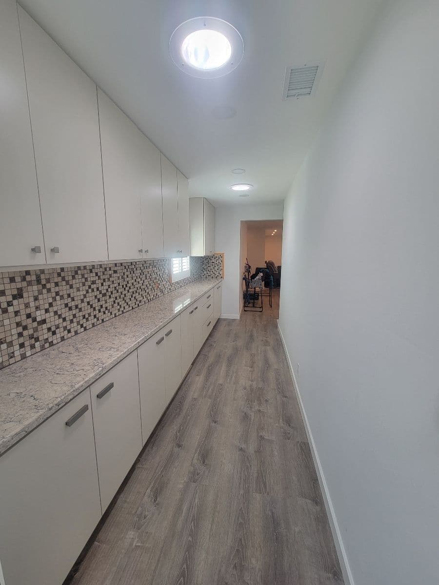 Narrow kitchen hallway with modern cabinets, tiled backsplash, and wood flooring.