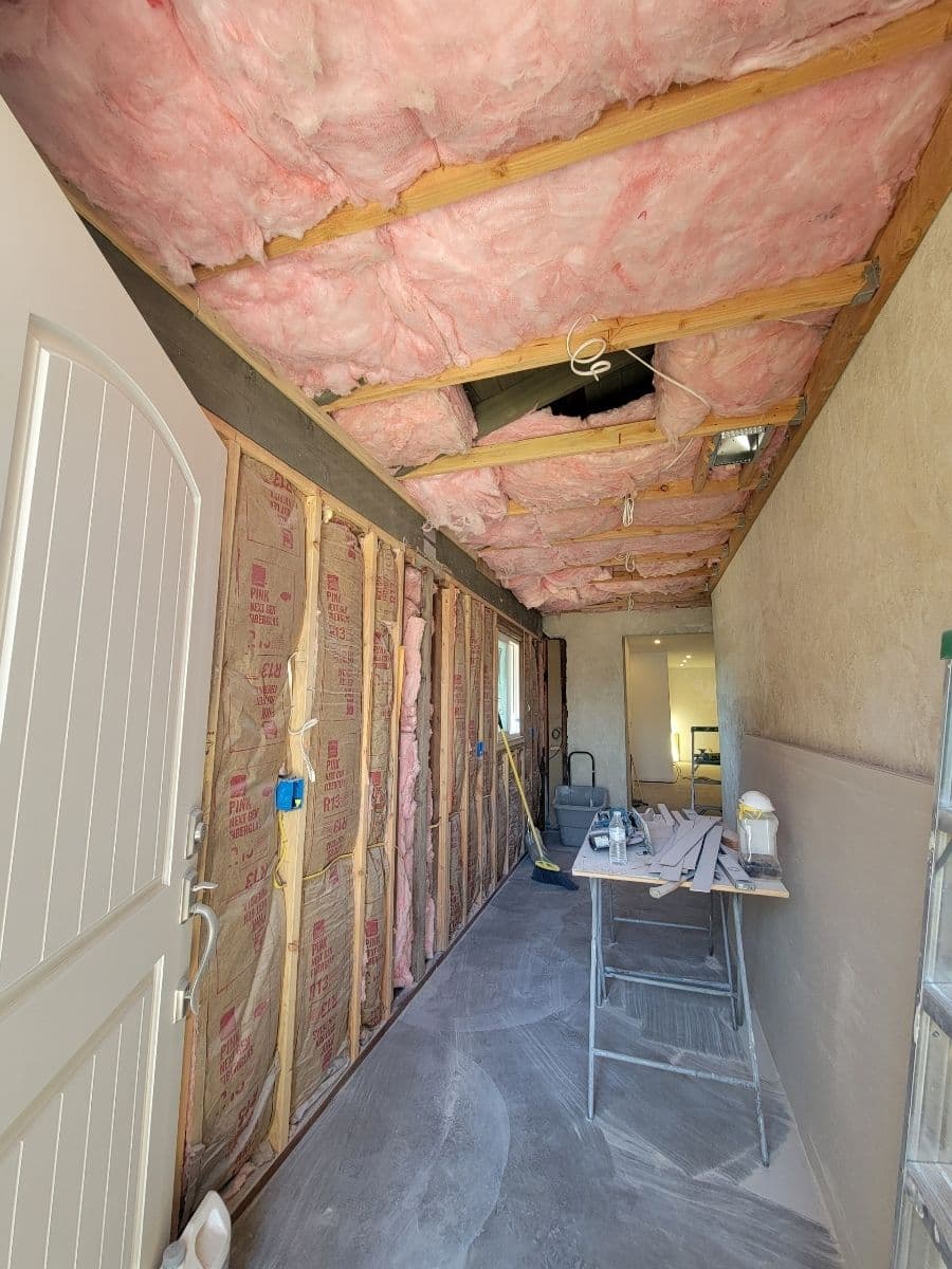 Interior renovation showing pink insulation, exposed walls, and construction tools in a hallway.