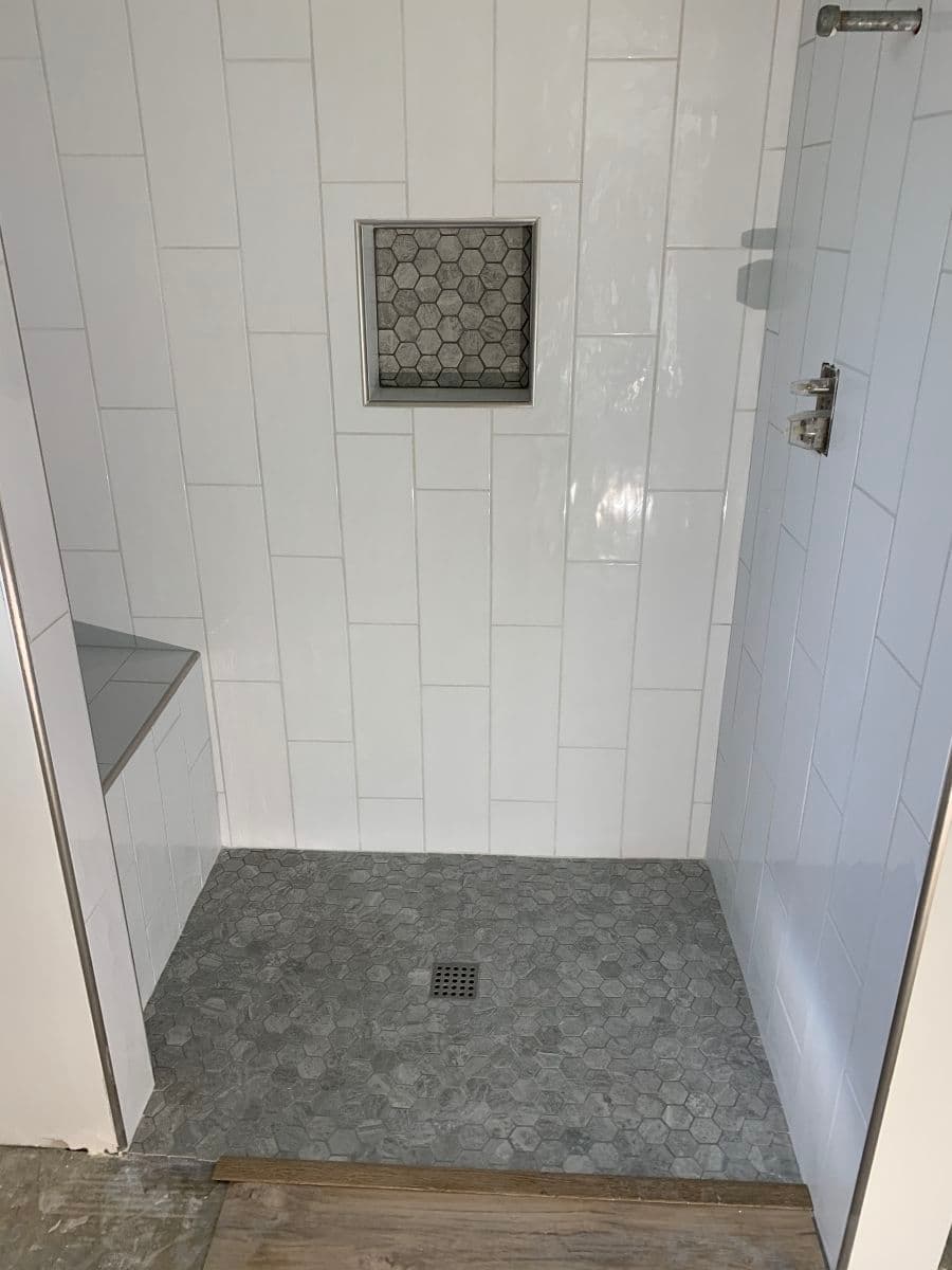 Modern shower design featuring white tiles, a gray hexagon floor, and built-in niche.