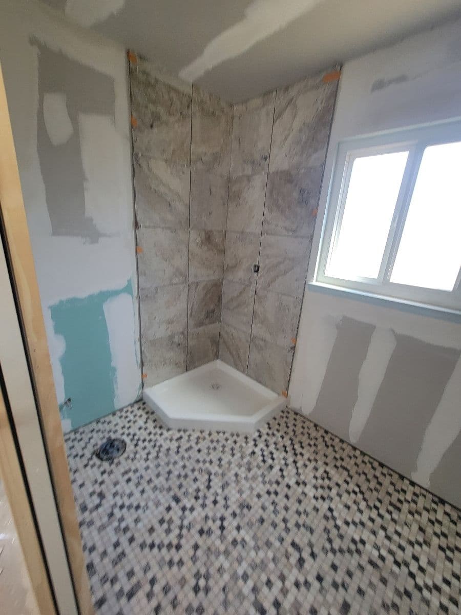 Renovated bathroom shower area with marble walls and mosaic floor, window for natural light.