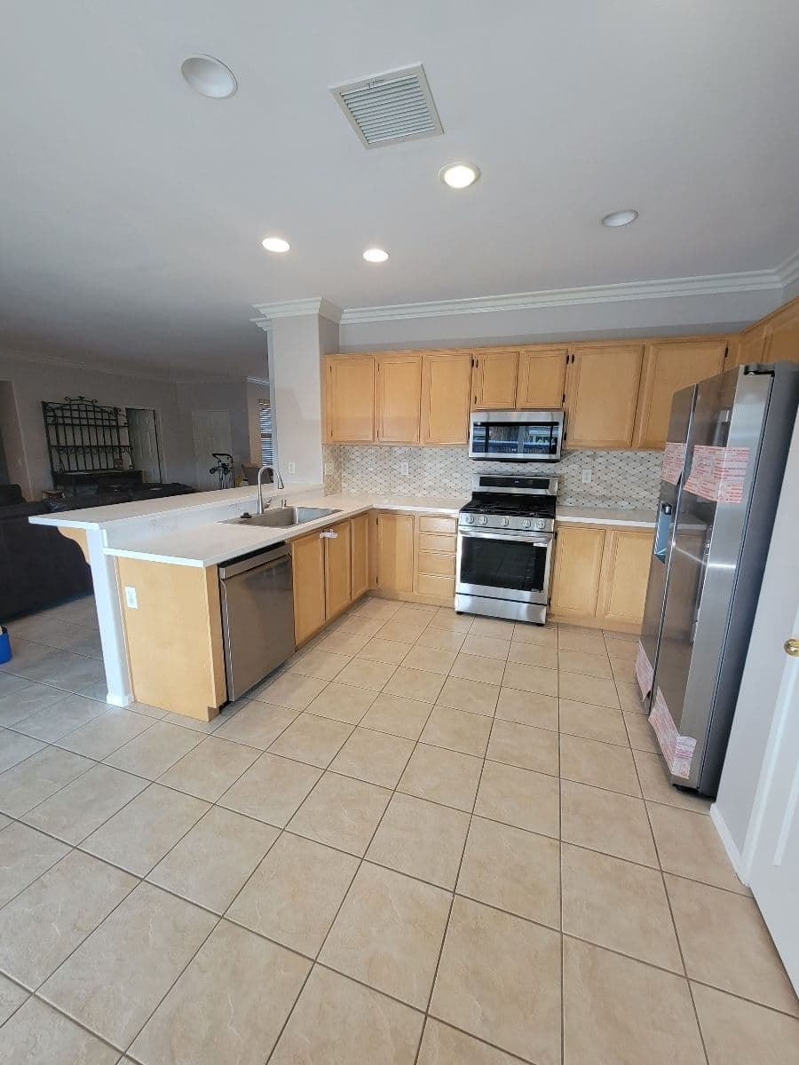 Modern kitchen with wooden cabinets, stainless steel appliances, and tile flooring.