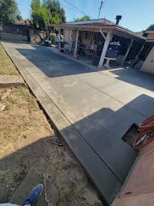 Freshly poured concrete driveway with a residential garage and landscaped yard in the background.