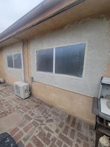 Exterior home walls with partially covered windows and air conditioning unit on a brick patio.