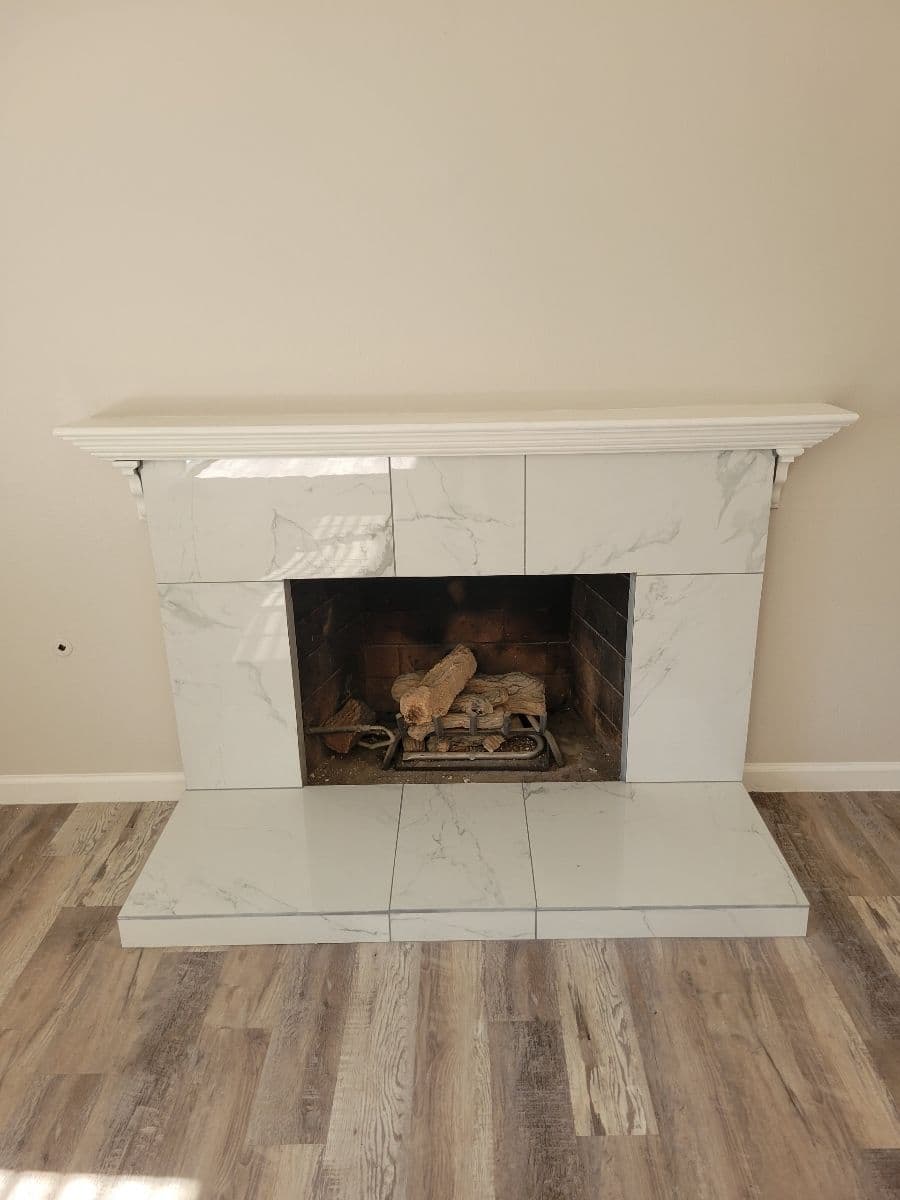 Modern marble fireplace with logs, surrounded by light-colored walls and wood flooring.