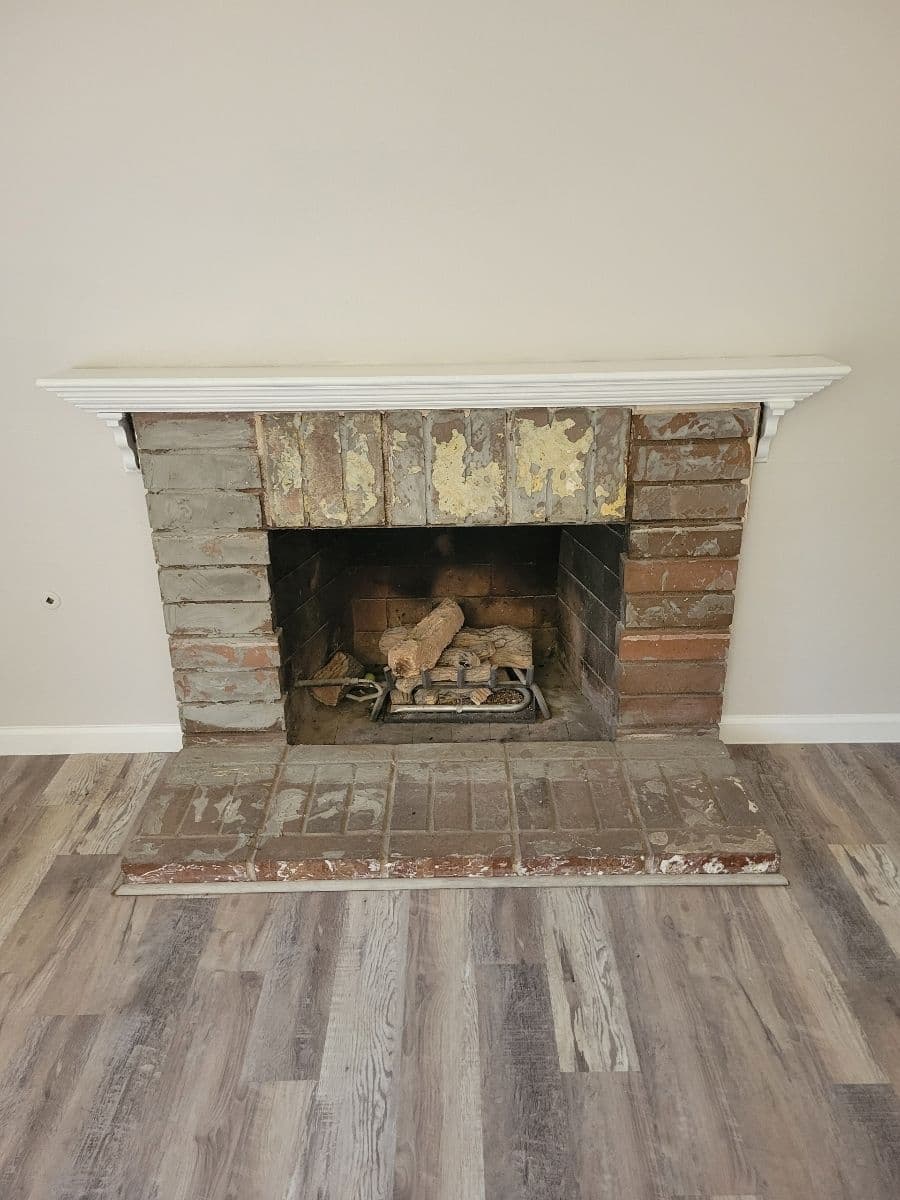 Old brick fireplace with peeling paint and exposed bricks in a minimalist room.
