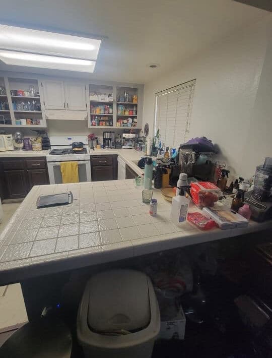 Bright kitchen with tiled countertop, shelves filled with kitchenware, and various appliances.