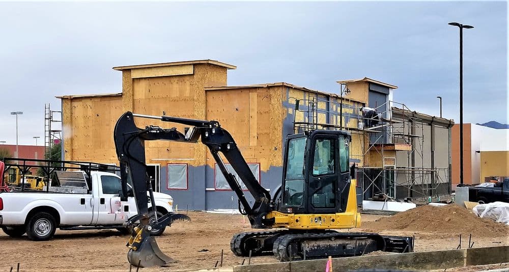 Construction site with an excavator in front of a building under renovation.