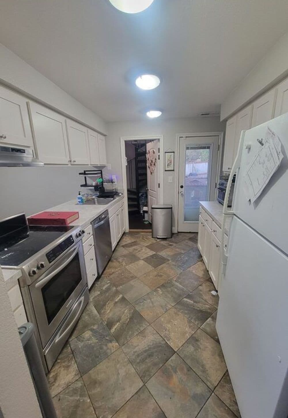 Modern kitchen with white cabinets, stainless steel appliances, and tiled floor.