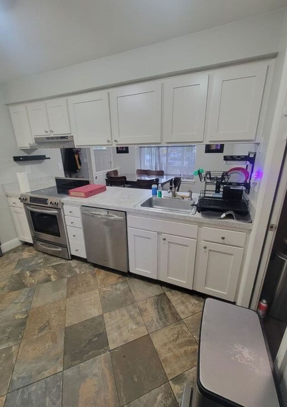 Modern kitchen with white cabinets, stainless steel appliances, and stone tile flooring.
