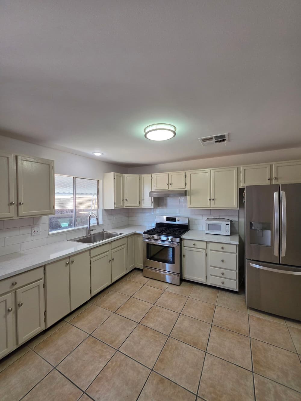 Modern kitchen with cream cabinets, stainless steel appliances, and tile flooring. Bright natural light.