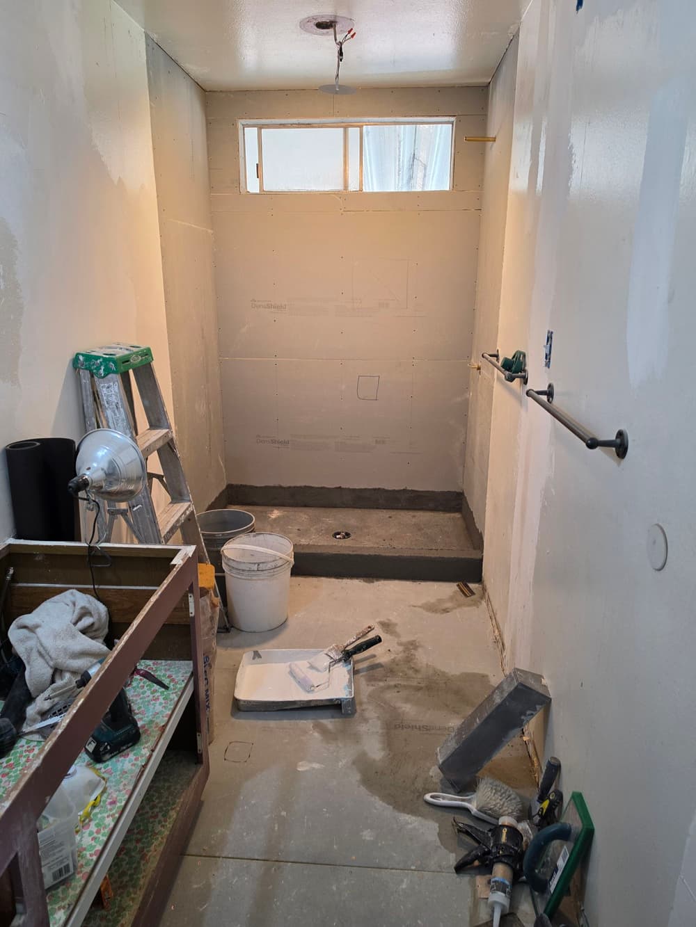 Renovation progress in a bathroom with tools, wall framing, and a shower base installation.