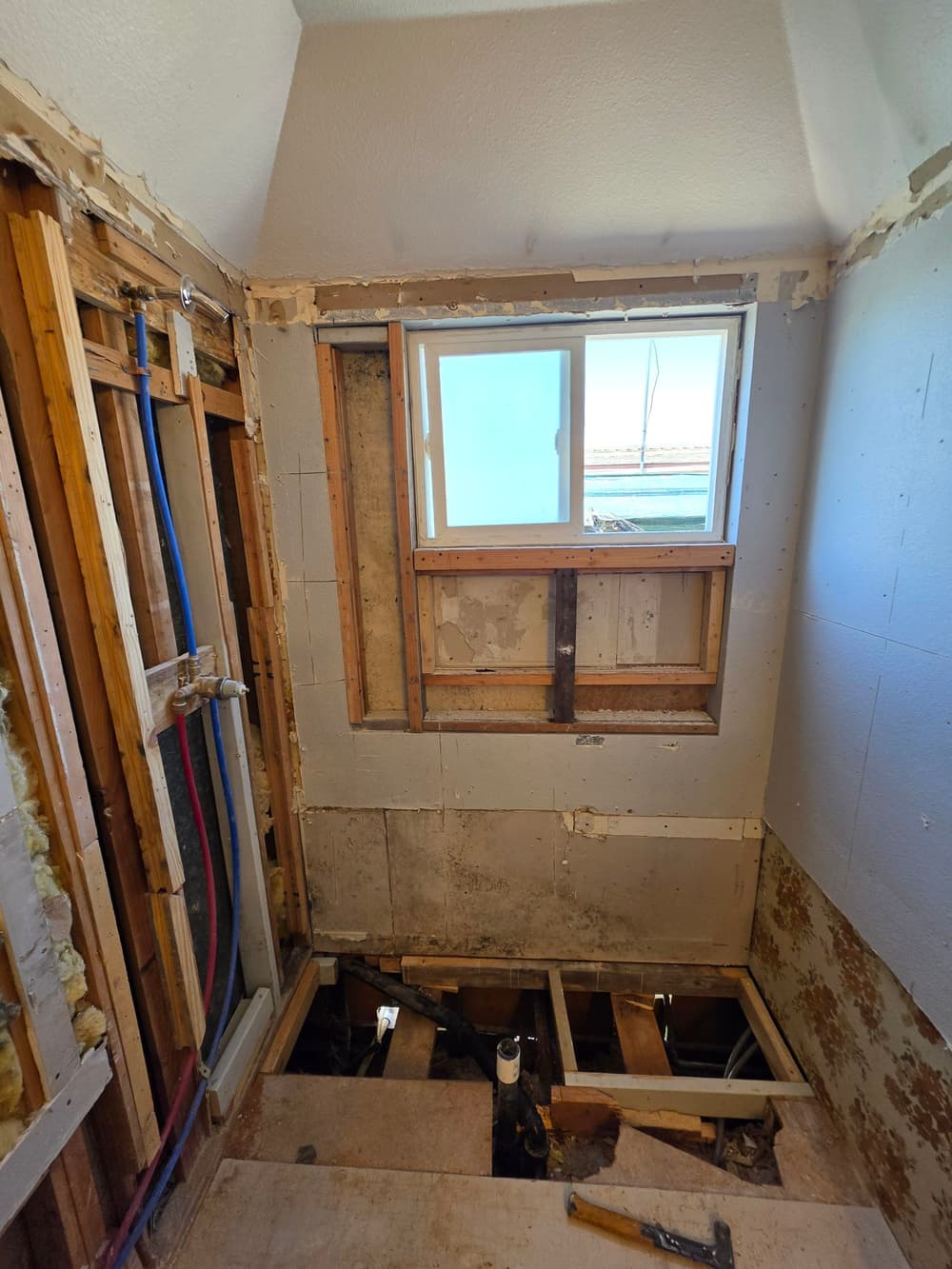 Renovation progress of a bathroom with exposed framing and newly installed window.